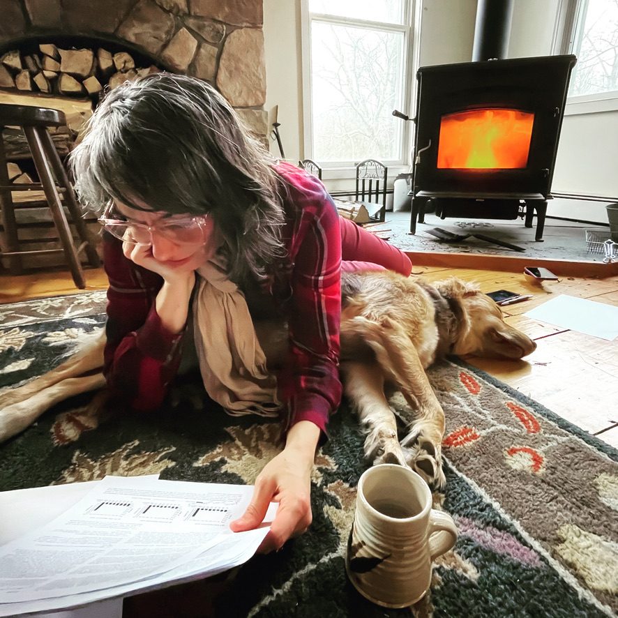 Camille reading research papers on a rug by the woodstove with her golden retriever