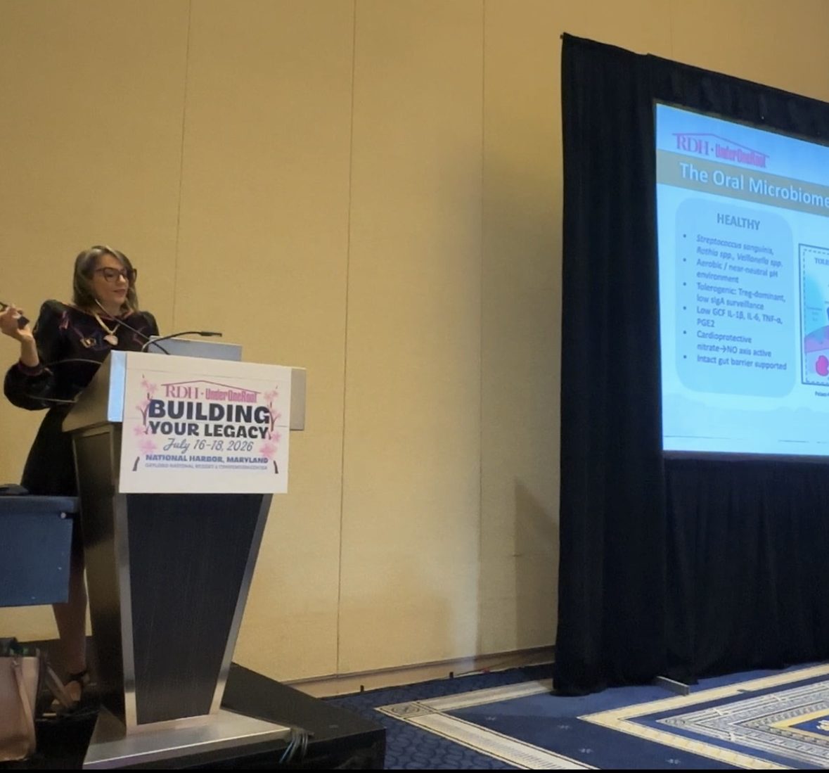 Camille at the podium at RDH Under One Roof 2026, presenting a slide on the healthy oral microbiome